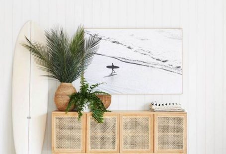 Beautiful beachy vibe with a cane console table in light wood, vertical white shiplap, large wall art, plants, and a surfboard! #entrywaydecor #foyerdecor #modern #coastal